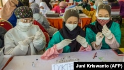 Dokter menyiapkan jarum suntik untuk diisi dengan vaksin Sinovac di Surabaya, Jawa Timur, pada 6 Juli 2021. Pemerintah mewacanakan untuk hanya mengizinkan dokter dan dokter gigi melakukan praktik di satu tempat saja atau disebut monoloyalitas. (Foto: AFP/Juni Kriswanto)