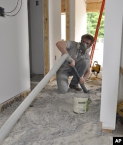 Addison Godine sprays insulation made from shredded, recycled newspaper in the team’s house.