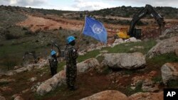 Pasukan penjaga perdamaian PBB memegang bendera sambil mengamati alat berat Israel mencoba menghancurkan terowongan yang dibangun Hizbullah dekat perbatasan Lebanon-Israel di Desa Mays al-Jabal, 13 Desember 2018. 