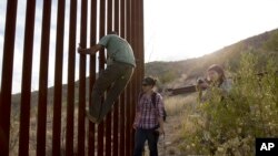 Mantan mandor konstruksi pagar perbatasan, Tim Foley menunjukkan bagaimana memanjat bagian dinding perbatasan yang memisahkan Meksiko dan Amerika Serikat kepada dua orang wartawan, 11 Mei 2016 (Foto: dok). 