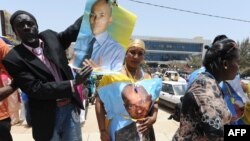 Members and supporters of the Parti Democratique Senegalais (PDS) hold a poster showing their leader, former Senegalese president Abdoulaye Wade and his son Karim, as they rally in front of the party's headquarters in Dakar, Apr. 23, 2014.
