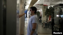 Seorang pekerja memeriksa tubuh pengunjung sebagai tindakan pencegahan di tengah persiapan pembukaan kembali pusat bisnis menyusul pandemi virus corona di Santiago, Chili, 29 April 2020. (Foto: Reuters)