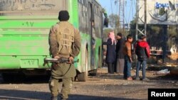 A rebel fighter stands with his weapon near evacuees from the Shi'ite Muslim villages of al-Foua and Kefraya as they ride buses in insurgent-held al-Rashideen, Syria, Dec. 20, 2016.