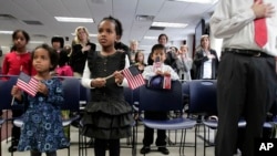 Dua perempuan bersaudara yang diadopsi di Ethiopia memegang bendera saat mereka mendengarkan lagu kebangsaan pada upacara hari adopsi di New York, 18 November 2010. (Foto: dok)
