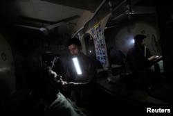 Seorang tukang cukur bekerja sambil mengigit lampu darurat saat mati lampu di kawasan miskin di Karachi, Pakistan