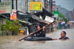 Seorang perempuan menggunakan rakit dari ban mengarungi banjir setelah hujan deras menyebabkan banjir di Bekasi, Jawa Barat, 1 Januari 2020. (Foto: AFP)