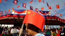 A Cambodian woman holds a Chinese flag as she walks a friendship bridge between Cambodia and China during its inauguration ceremony in Takhmao, Kandal provincial town, south of Phnom Penh, Cambodia, Monday, Aug. 3, 2015. 
