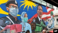 Sepasang suami istri Melayu makan siang di samping lukisan mural sebagai penghormatan untuk pekerja medis Malaysia dalam melawan virus corona Covid-19 di Damansara di Selangor, di luar Kuala Lumpur, Malaysia, 7 November 2020. (Foto: AP)