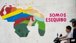 Warga melintas melewati mural bergambar wilayah Essequibo yang terpampang di salah satu sudut Caracas, Venezuela, pada 11 Desember 2023. (Foto: AP/Matias Delacroix)