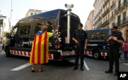 A woman with an ''estelada'' or Catalonia independence flag places a carnation on a vehicle belonging to police officers from Mossos d'Esquadra in Barcelona, Spain, Sept. 24, 2017.