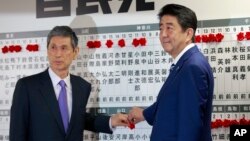 Japanese Prime Minister Shinzo Abe, right, leader of the Liberal Democratic Party, poses with vice president Masahiko Komura for photos as he marks on the name of one of those elected in the parliamentary lower house election at the party headquarters in Tokyo, Sunday, Oct. 22, 2017. 