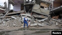 Wafaa Abdelhadi melintasi reruntuhan rumah yang hancur akibat serangan Israel bersama putrinya, Lynn dan Roueida, setelah vaksinasi polio di Deir Al-Balah, Gaza Tengah, 1 September 2024. (Foto: Ramadan Abed/Reuters)