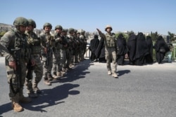 Turkish soldiers stand guard on a bridge overlooking a section of the M4 highway, which links provinces of Aleppo and Latakia, while Syrian women gather to throw stones at a joint Russian-Turkish military convoy near Ariha in Syria's rebel-held northwestern Idlib province, on June 10, 2020