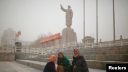 Ethnic Uighurs sit near a statue of China's late Chairman Mao Zedong in Kashgar, Xinjiang Uighur Autonomous Region, China, March 23, 2017. 