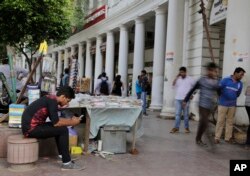 FILE - An Indian man, left, uses his mobile phone as people walk past in New Delhi, India.