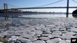 A layer of ice is broken into pieces floating along the banks of the Hudson River at the Palisades Interstate Park with the George Washington Bridge in the background, Jan. 2, 2018, in Fort Lee, New Jersey.