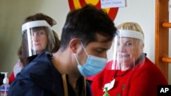 13일 러시아 루폴로포 마을에 마련된 지방선거 투표소에서 신종 코로나바이러스 방역을 위해 안면보호대를 착용한 선거관계자들이 한 유권자가 투표하는 모습을 지켜보고 있다.