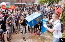 FILE - In this Aug. 12, 2017 file photo, white nationalist demonstrators, right, clash with a counter demonstrator as he throws a newspaper box at the entrance to Lee Park in Charlottesville, Va.