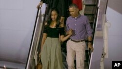Presiden AS Barack Obama menggandeng putrinya Sasha, diikuti istrinya Michelle dan putrinya Malia, menuruni pesawat Air Force One setibanya di Honolulu untuk liburan tahunan mereka (16/12). (AP/Marco Garcia)