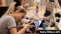 In this Sunday, April 22, 2018 photo, Washington Square News fashion blog editor Amanda Burkett checks images on her camera while working on deadline at the independent, student-run newspaper in New York.