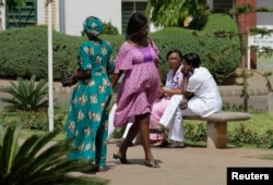 FILE - A pregnant woman walks past health care workers outside the hospital in Abuja, Nigeria, March 5, 2013.