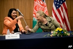 FILE - U.S. Secretary of State Hillary Clinton, right, helps Samira Hamidi, an Afghan rights advocate, with a microphone during the Afghan Civil Society event in Tokyo, July 8, 2012.