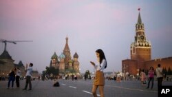 Seorang wanita muda memegang telepon genggamnya di Lapangan Merah dengan latar belakang Menara Spasskaya Kremlin (kanan) dan Katedral St. Basil (tengah) di latar belakang di Moskow, Rusia, Senin, 25 Juli 2016. (AP Photo / Pavel Golovkin)