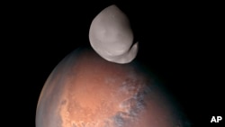 This composite image provided by the UAE Space Agency shows Mars’ moon Deimos in the foreground. The colors were derived from images captured in different wavelengths.