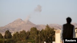 A man looks on as smoke billows from military barracks in the Jabal al-Jumaima mountain following an airstrike near Sana'a, Yemen, March 30, 2015. 
