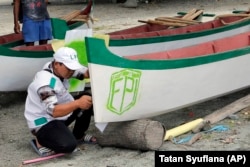 In this April 2, 2019, photo, a member of Islamic Defenders Front paints their group's logo as they help local fishermen to build boats at a fishing village affected by the 2018 tsunami in Palu, Central Sulawesi, Indonesia.