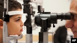 In this file photo, Dr. Albert Maguire (R), at the Children's Hospital of Philadelphia, checks the eyes of Misa Kaabali, 8, who was 4-years-old when he received his gene therapy treatment, Oct. 4, 2017.
