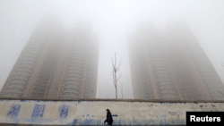FILE - A woman wearing a mask walks past buildings on a polluted day in Handan, Hebei province, China, Jan. 12, 2019. China is reportedly the world's top emitter of greenhouse gases.