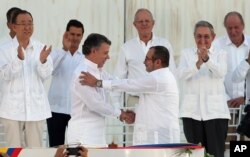 Colombia’s President Juan Manuel Santos, front left, and the top commander of the Revolutionary Armed Forces of Colombia (FARC) Rodrigo Londono shake hands after signing the peace agreement.