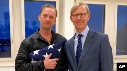 FILE - In this image provided by the U.S. State Department, Michael White holds an American flag as he poses for a photo June 4, 2020, with U.S. special envoy for Iran Brian Hook at the Zurich, Switzerland, airport after White’s release from Iran.