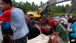 Rescuers sit beside a body bag containing the remains of a civilian victim when a Philippine military C-130 plane crashed in Patikul town, Sulu province, southern Philippines on July 4, 2021. 