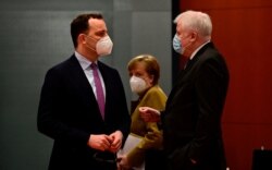 German Chancellor Angela Merkel, center, looks on as Health Minister Jens Spahn, left, and Interior Minister Horst Seehofer talk prior to the weekly cabinet meeting in Berlin, March 17, 2021.