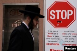 A man walks past a sign advising about a measles outbreak in the Brooklyn borough of New York, April 25, 2019.
