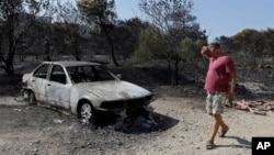 A man looks at a burned-out car during a wildfire near Kalyvia in Greece, Aug. 3, 2017. 