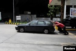 Attendants push a car at a gas station of Venezuelan state-owned oil company PDVSA in Caracas, Venezuela, Sept. 21, 2017.