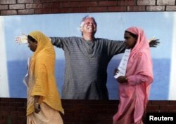 Karyawan Grameen Bank berjalan di depan potret peraih Nobel Muhammad Yunus di Dhaka, 8 Maret 2011. (Foto: Reuters)