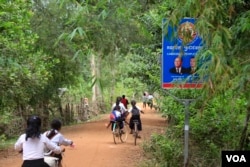 Children ride their bicycles past a sign bearing the Cambodian People's Party logo and the faces of Prime Minister Hun Sen and National Assembly President Heng Samrin in Banteay Meas village, Taches commune, Kampong Chhnang province. Although village officials are supposed to be politically neutral, the chief of Banteay Meas is registering villagers as CPP members. "We just want to look for people who are honest with the party," said the chief, Nguon Korn. (Sun Narin/VOA Khmer)