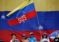 FILE - A supporter of Venezuela's opposition leader and self-proclaimed interim president, Juan Guaidó, waves a Venezuelan flag marked with the letters "SOS" during a rally in Caracas, Venezuela, May 11, 2019.