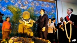 Cambodian Deputy Prime Minister Sok An, center, stands next to a 10th century Cambodian sandstone statue as the Director of the Cleveland Museum of Art William M. Griswold, right, holds a garland during a ceremony in Phnom Penh, Cambodia.