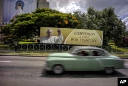 A man drives a vintage American car next to a display — which reads "Welcome to Cuba Pope Francis" in Spanish — at Revolution Square in Havana, Cuba, Sept. 15, 2015.