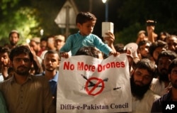 FILE - A boy holds a banner while sitting on his father's shoulder attending a rally called by Pakistan Defense Council, a coalition of Islamic parties, in Lahore, Pakistan, June 12, 2016.