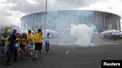 Soccer fans walk away from a cloud of tear gas as riot police clash with demonstrators outside the Mane Garrincha National Stadium in Brasilia, June 15, 2013.
