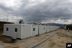 A worker walks next to container houses at a new refugee camp in the town of Thiva, about 90 kilometers (56 miles) north of Athens, , March 14, 2017. The old textile factory will host 700 people and will open for the refugees and migrants in the next days.