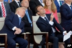 FILE - Then-U.S. President Donald Trump and French President Emmanuel Macron watch the traditional Bastille Day military parade, including military jet flyovers, on the Champs Elysees in Paris on July 14, 2017.