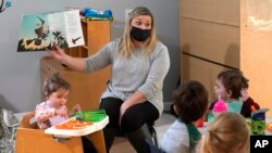 Amy McCoy reads a book to preschoolers as they finish their lunch at her Forever Young Daycare facility, Monday, Oct. 25, 2021, in Mountlake Terrace, Wash. (AP Photo/Elaine Thompson)