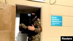 A still image taken from video shows a masked law enforcement officer addressing journalists during a raid in a local office of Kremlin critic Alexei Navalny, in Perm, Russia, Sept. 12, 2019.
